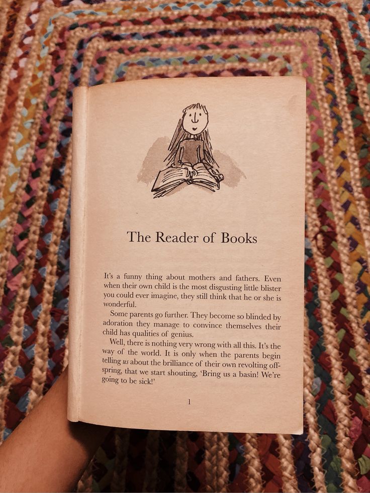 the reader of books is holding up an open book on top of a multicolored rug