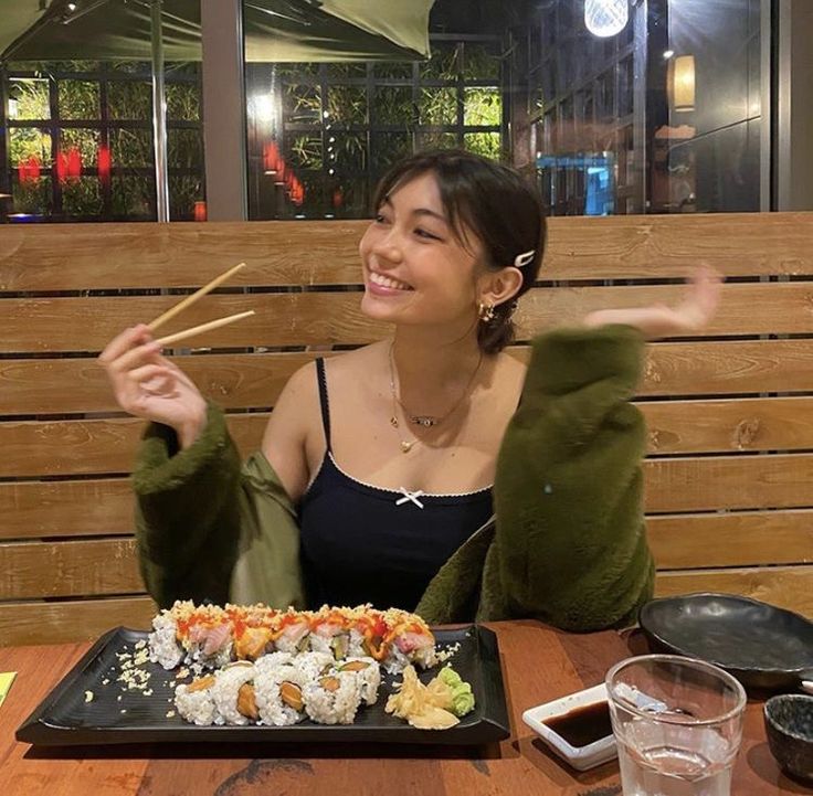 a woman sitting at a table with sushi and chopsticks in front of her