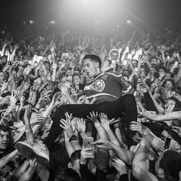 a man sitting on top of a crowd of people in front of an audience at a concert