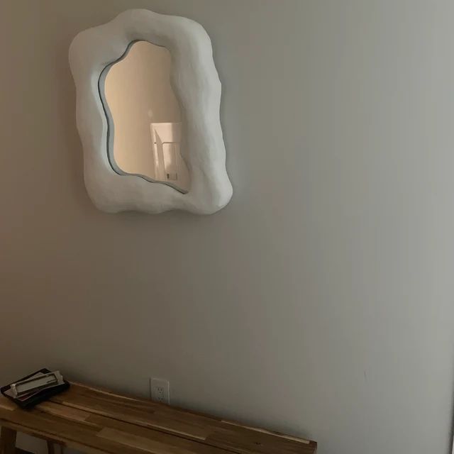 a mirror hanging on the wall above a wooden bench in a room with white walls