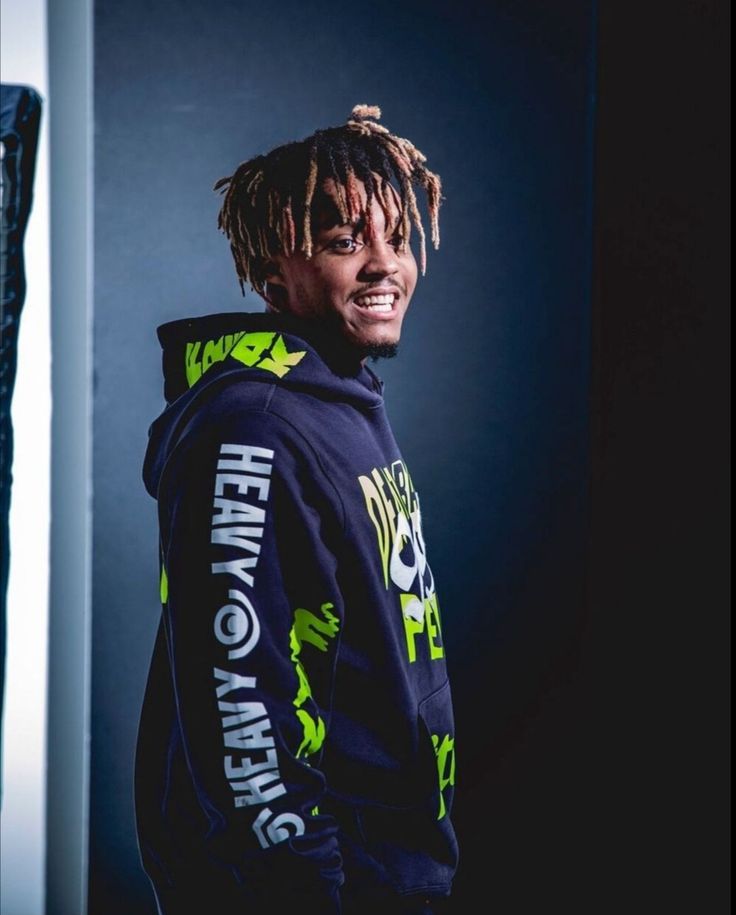 a man with dreadlocks standing in front of a wall wearing a hoodie