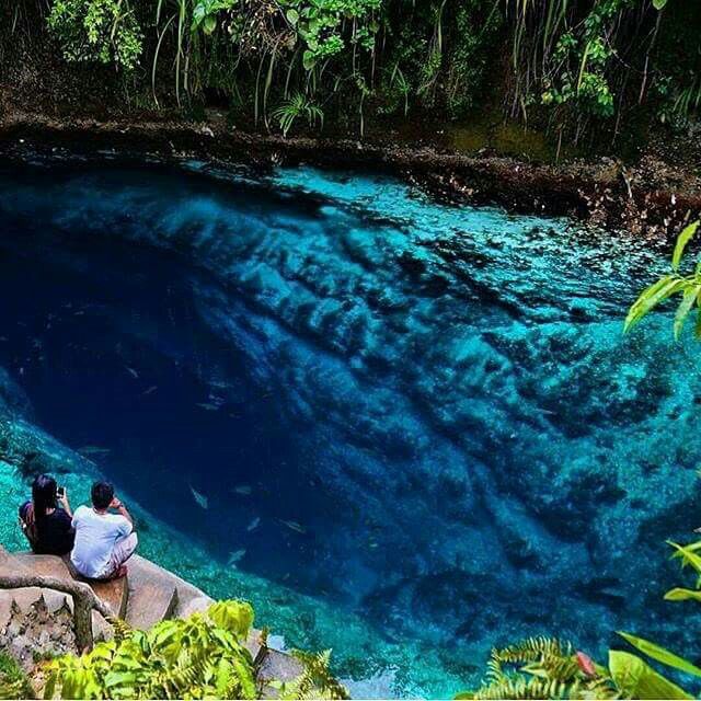 two people are sitting on the edge of a blue pool with fish swimming in it