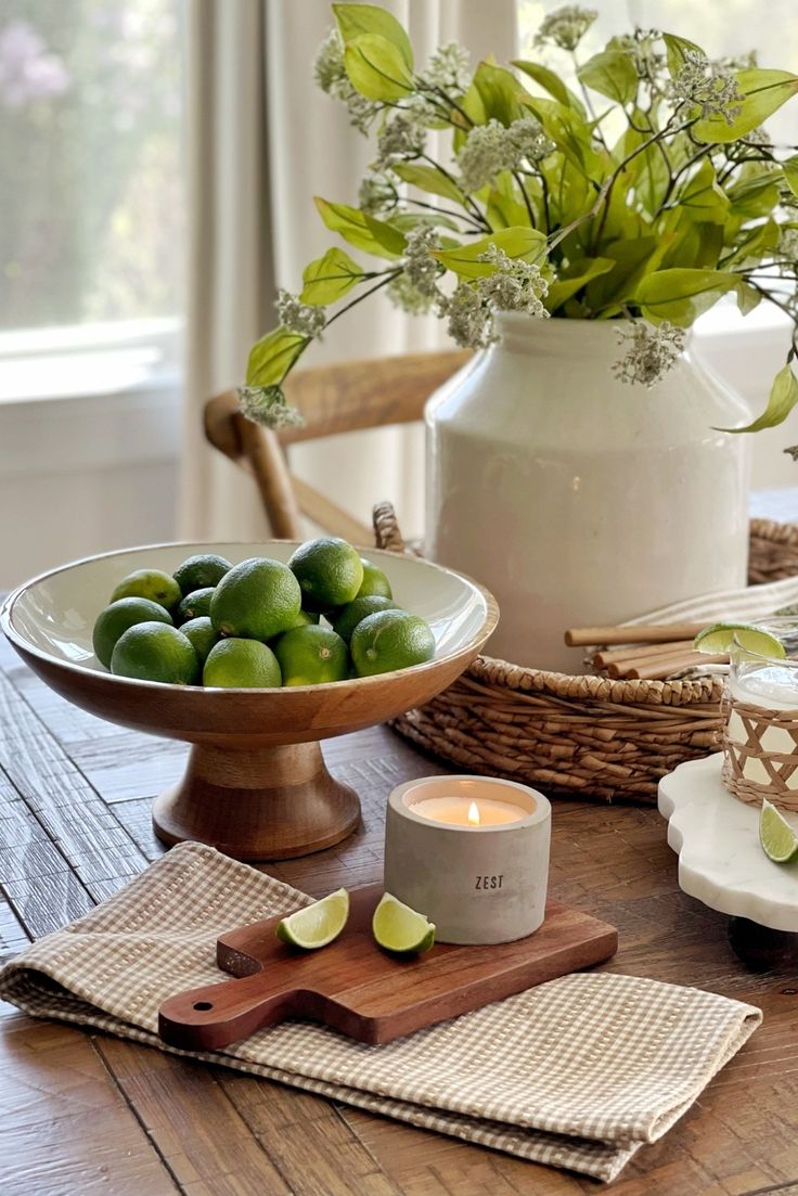 a table with limes and candles on top of it next to a vase filled with flowers