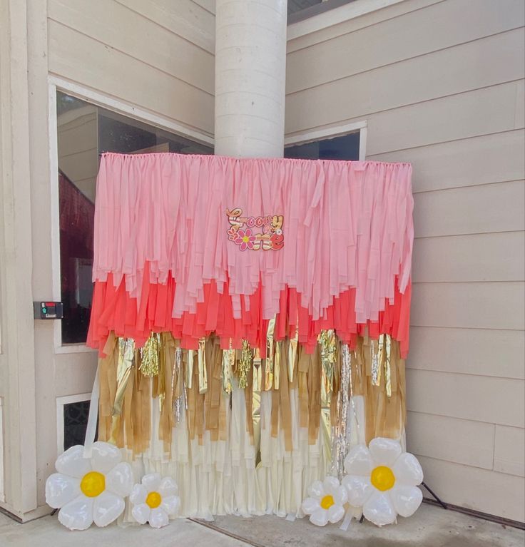 a pink and gold curtain on the side of a building with flowers in front of it