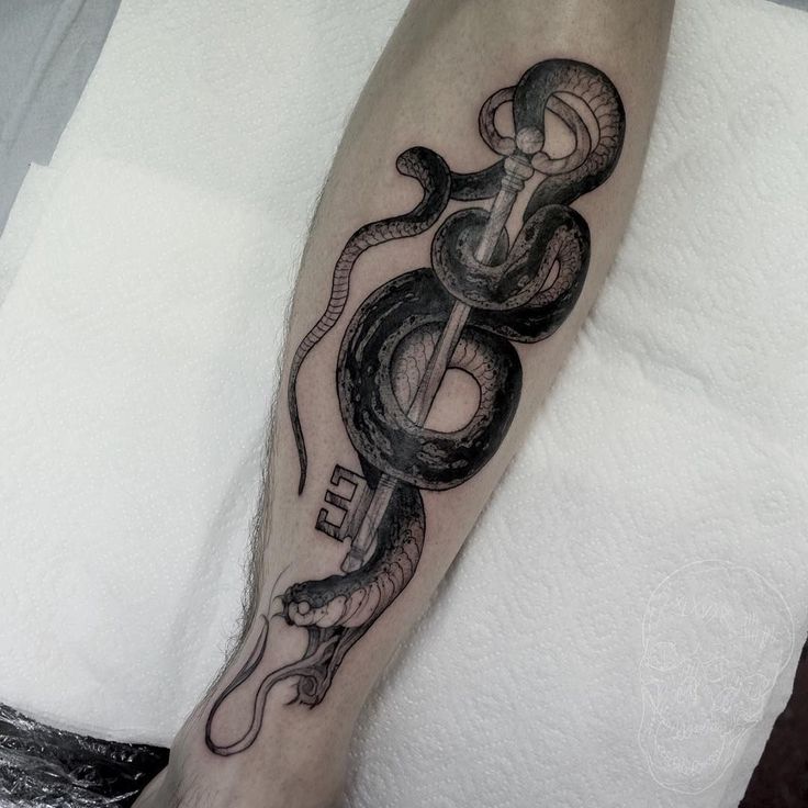 a black and grey snake tattoo on the left leg, with a key in it's mouth