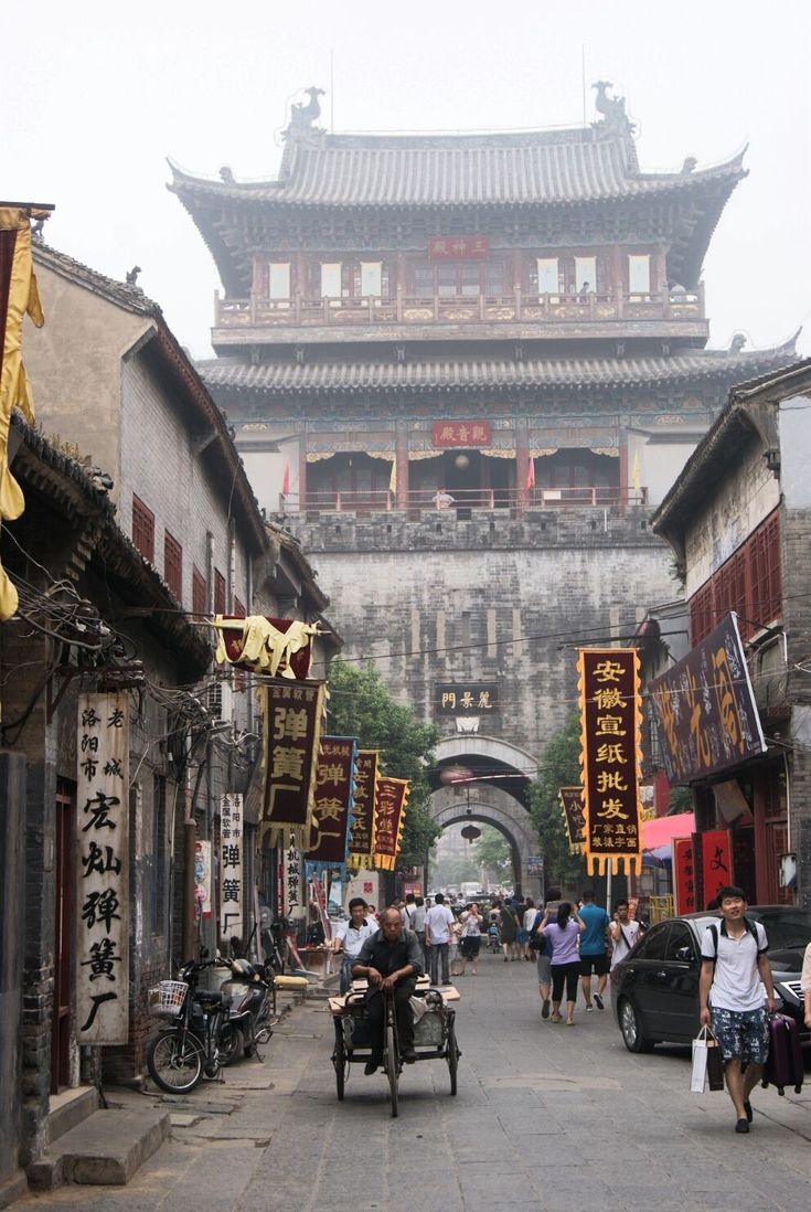 people walking down an alley way in front of buildings with chinese writing on the walls