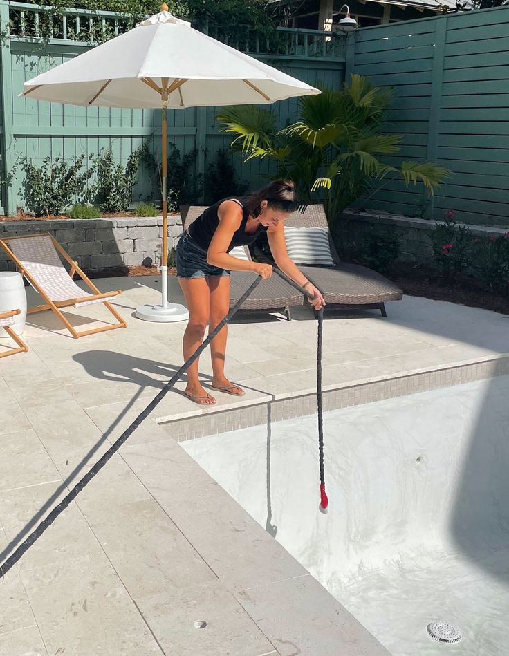 a woman is cleaning the pool with a large plunger and an umbrella over her head