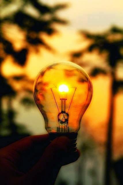 a person holding up a light bulb with the sun setting in the distance behind them