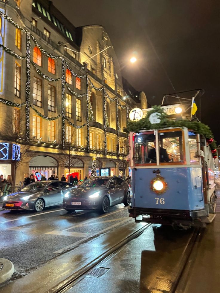 a trolley car driving down the street in front of a building with christmas lights on it