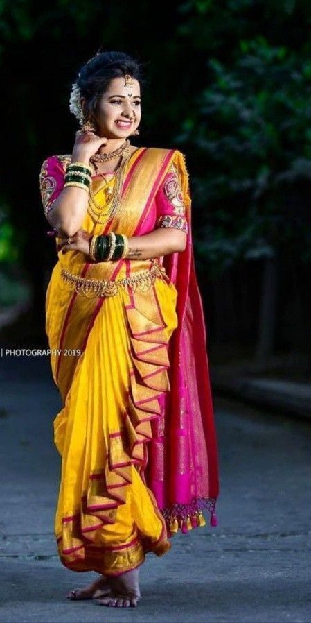 a woman in a yellow and pink sari is standing on the street with her arms crossed