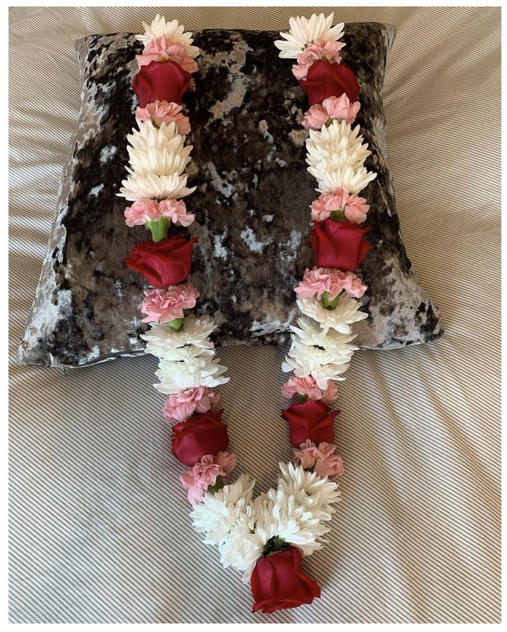 a decorative letter made out of flowers on top of a bed with a pillow behind it