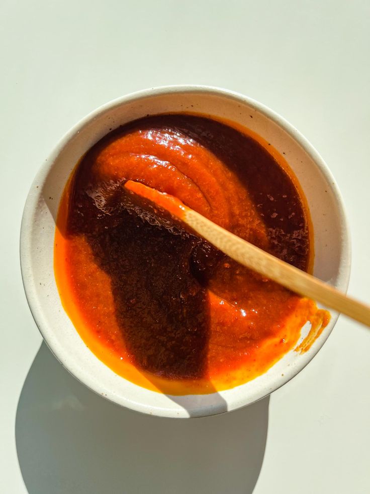 a white bowl filled with red sauce and a wooden spoon sitting on top of it