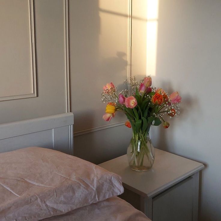 a vase filled with flowers sitting on top of a table next to a bed in a bedroom