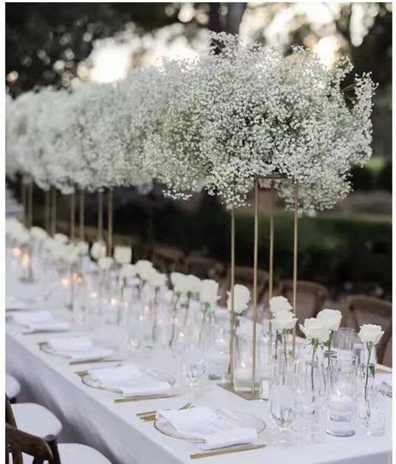 a long table with white flowers in vases and place settings on the tables are lined up