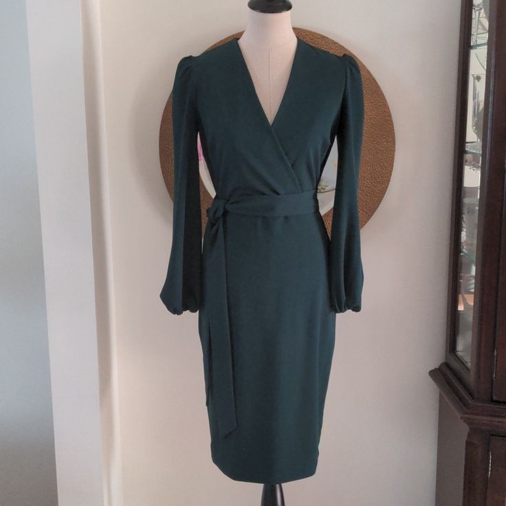 Classic Beauty Dress In A Gorgeous Evergreen By Alexa Admor. It Has A Beautiful V Crossover Neckline And Anp Attached Belt To Tie. The Shoulders Have A Gathered Puff And The Cuffs Are Covered Elastic. This Dress Can Be Worn For Numerous Occasions. Green Long Sleeve Midi Dress For Date Night, Chic Dark Green V-neck Dress, Fitted Green Long Sleeve Wrap Dress, Chic Olive V-neck Dress, Elegant Green Long Sleeve Wrap Dress, Chic Dark Green Knee-length Dress, Formal Dark Green V-neck Dress, Green Wrap Dress With Surplice Neckline For Party, Green Surplice Neckline Wrap Dress For Party