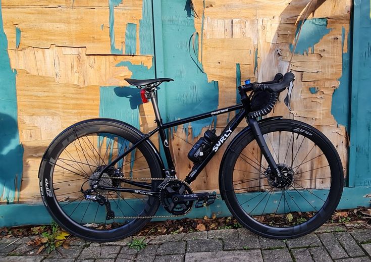 a black bike parked in front of a wooden wall with peeling paint on it's side