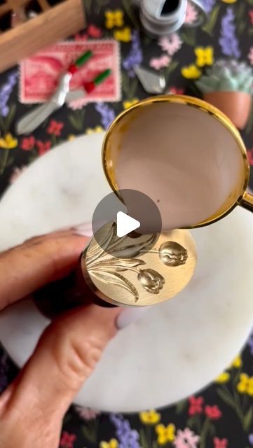 a person holding a gold ring on top of a white plate with flowers around it