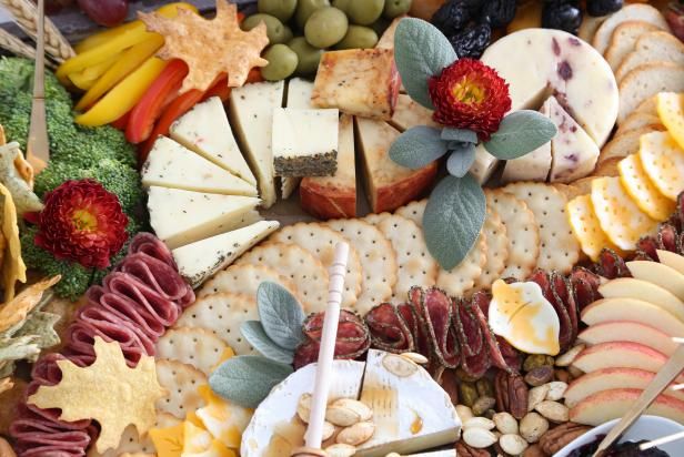 an assortment of cheeses, crackers and fruits on a platter with forks