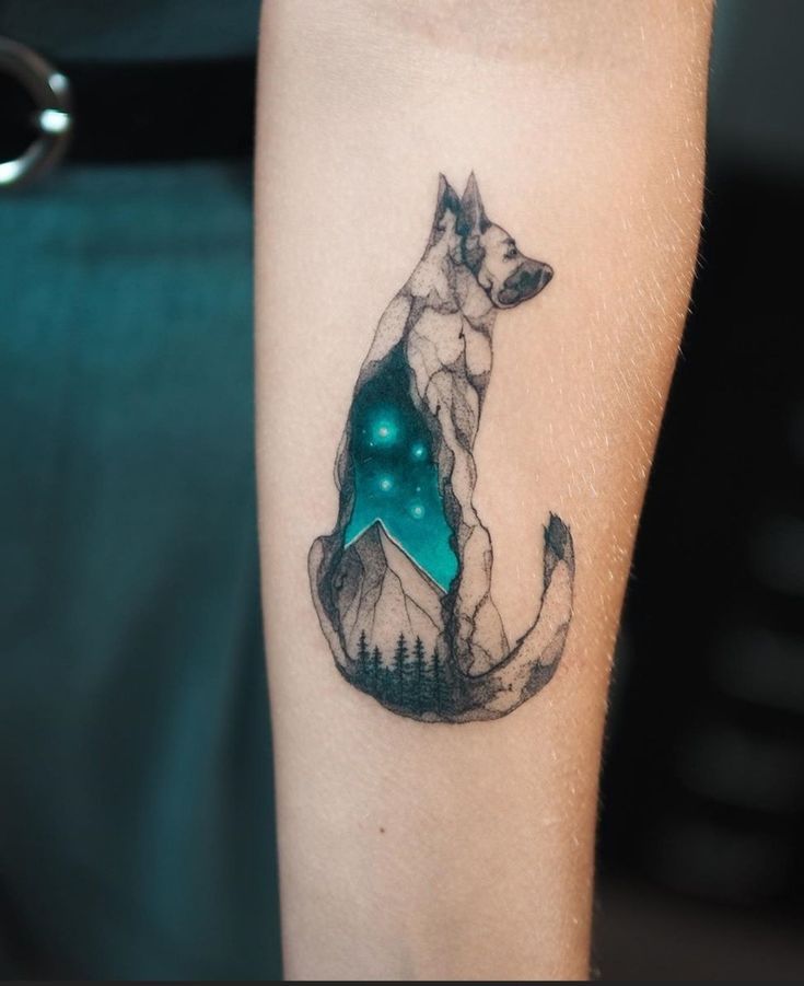 a person with a tattoo on their arm that has a dog and mountains in the background