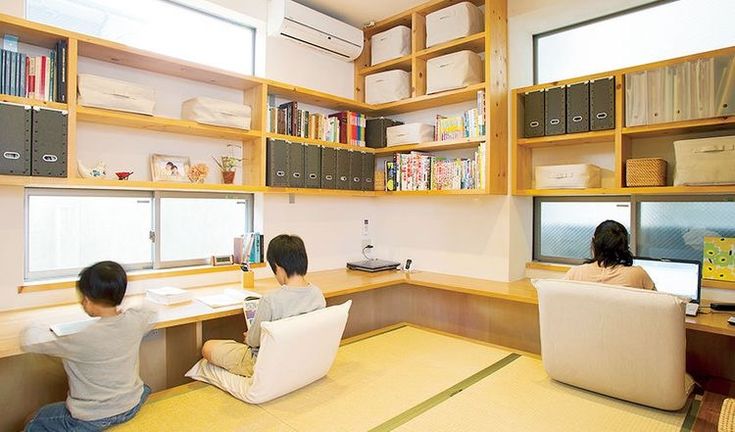 two people sitting at a desk in front of a computer monitor and bookshelf