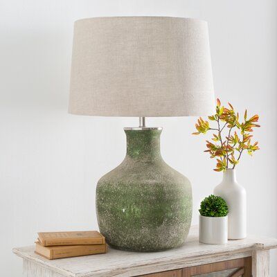 a green vase sitting on top of a wooden table next to a lamp and books