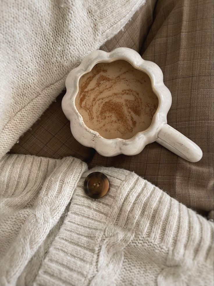 a cup of coffee sitting on top of a bed next to a white knitted blanket