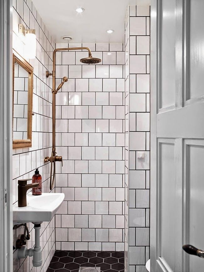 a white bathroom with black and white tile on the floor, shower head, sink and mirror