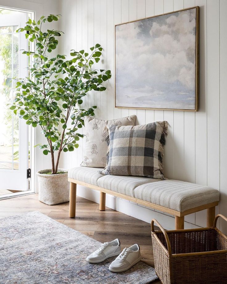 a white couch sitting next to a tree in front of a painting on the wall