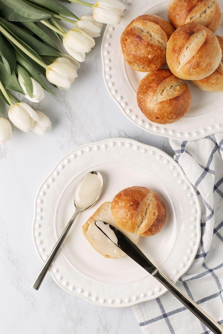 two white plates topped with pastries next to a bouquet of tulips and a spoon