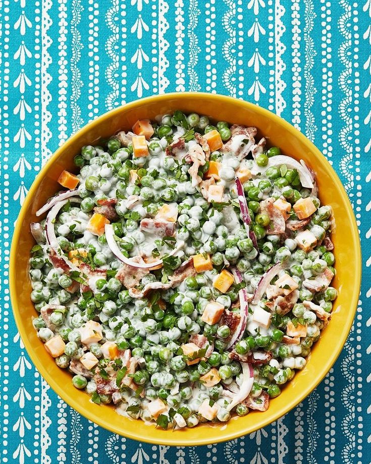 a yellow bowl filled with peas, onions and carrots on top of a blue tablecloth