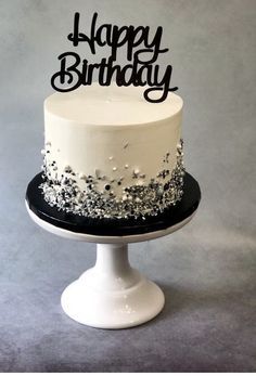 a white and black birthday cake sitting on top of a table with silver confetti