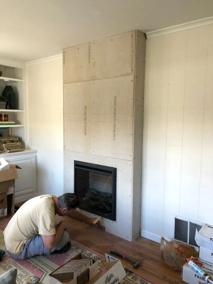 a man laying on the floor next to a fire place in a room with white walls