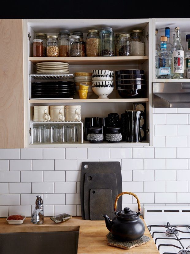 a kitchen with white tiles and wooden shelves filled with pots, pans, and other items