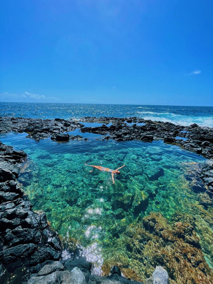 a person swimming in the ocean with rocks and clear blue water on either side of them