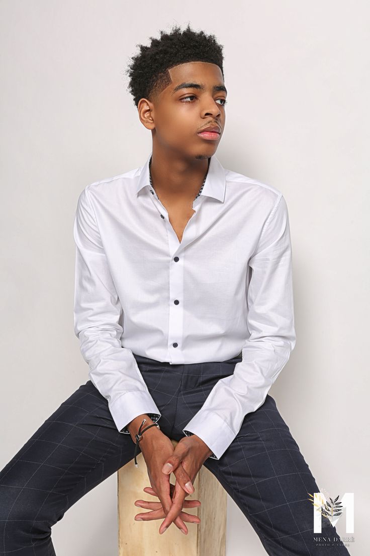 a young man sitting on top of a wooden block wearing a white shirt and black pants