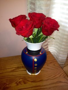 a blue and white vase with red roses in it