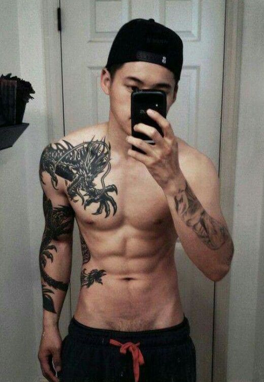 a shirtless man taking a selfie in the mirror with his cell phone and tattoo