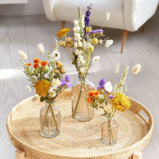 three vases filled with flowers sitting on top of a wicker table