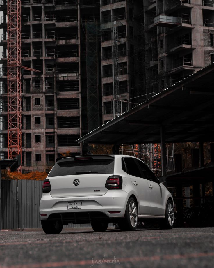 a white volkswagen car parked in front of a building under construction with cranes behind it