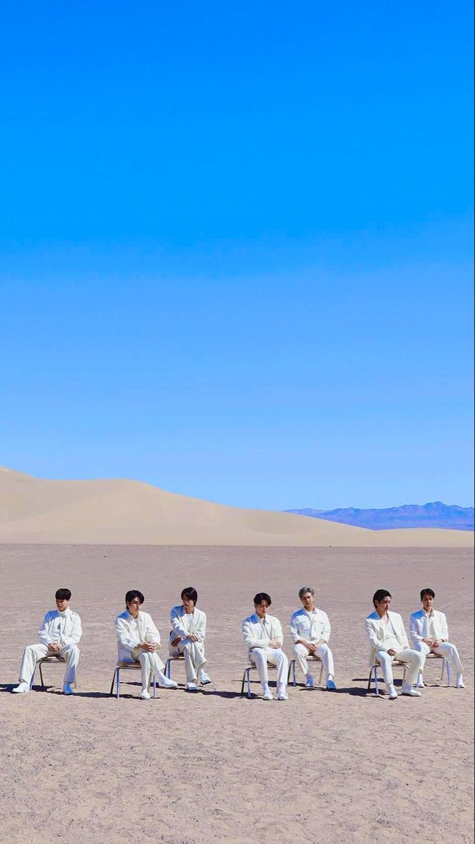 a group of men sitting on top of white chairs in the middle of a desert