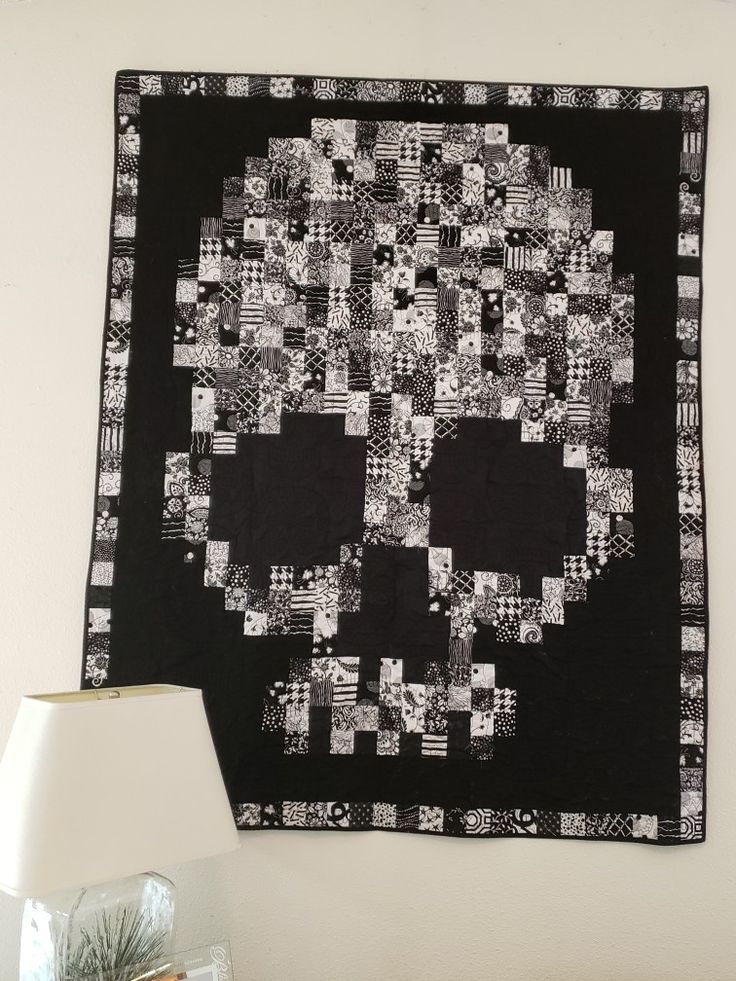 a black and white skull quilt hanging on the wall next to a table with a lamp