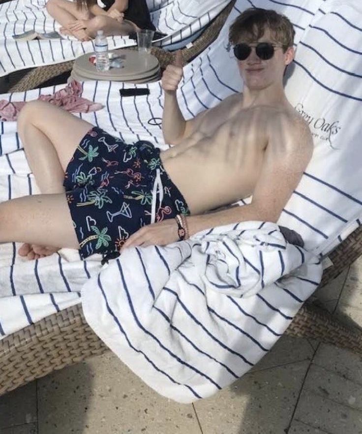 a man laying on top of a beach chair next to another person wearing sunglasses and holding a drink