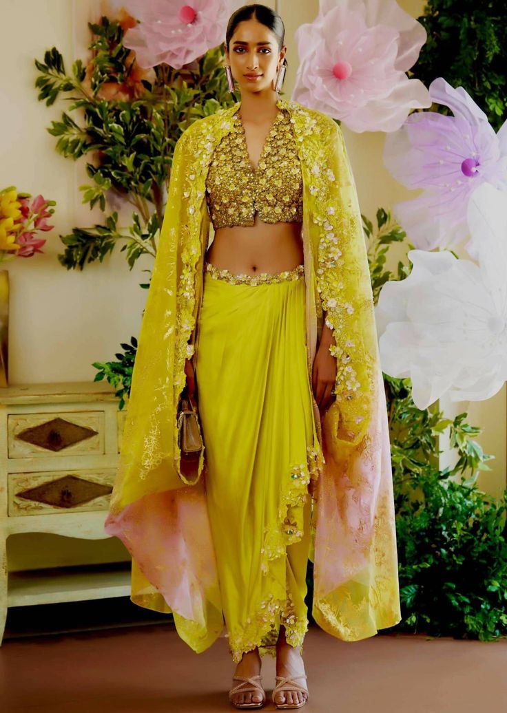 Shine bright like a diamond at this seasons soirees. The lime green set comes with a blouse covered with daisy flower applique work. The dhoti-style skirt also glamourizes the outfit with its asymmetrical look. The dupatta/cape that is paired with the outfit has an ombre effect to tie in all the colors of the embellish Navratri Draped Sets With Sheer Dupatta, Designer Wear Draped Sharara With Resham Embroidery, Cowl Skirt Outfit, Green Draped Lehenga With Cutdana, Draped Anarkali Sets For Festivals, Anarkali Draped Sets For Festivals, Designer Draped Traditional Wear With Resham Embroidery, Traditional Drape Sets With Gota Work For Reception, Reception Sets With Gota Work In Traditional Drape