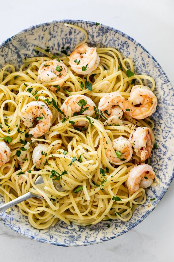 pasta with shrimp and parsley in a blue and white bowl on a marble table