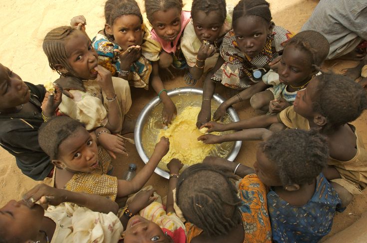 a group of children are gathered around a bowl of food