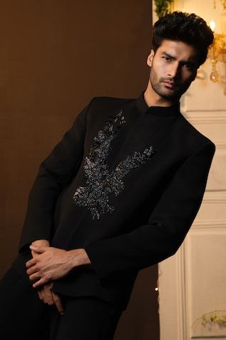 a man standing in front of a wall wearing a black shirt with silver flowers on it