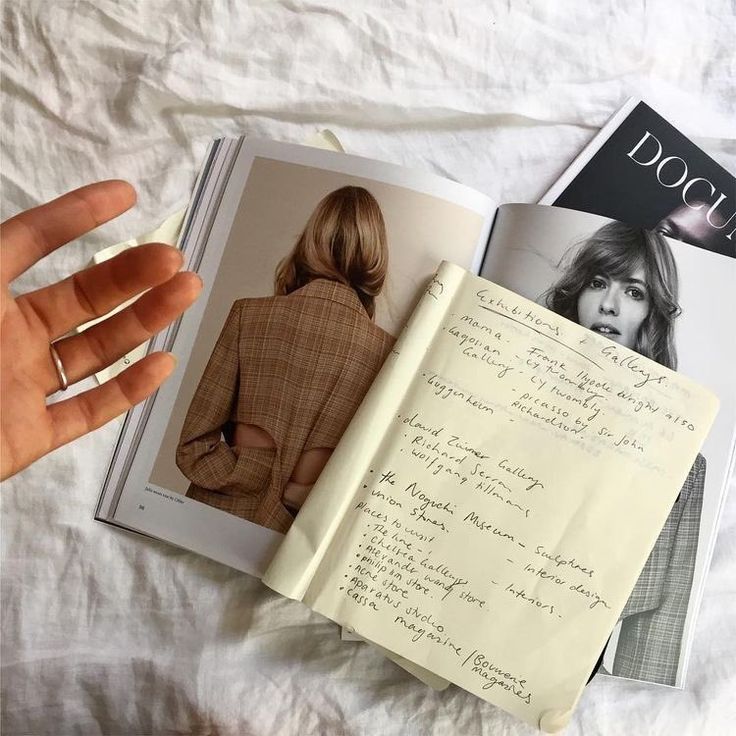 an open book with writing on it next to a hand holding a pen and paper