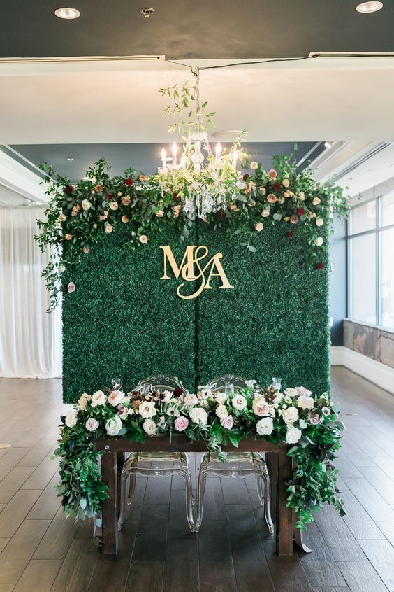 a table with flowers and greenery on it in front of a green wall that says m & a