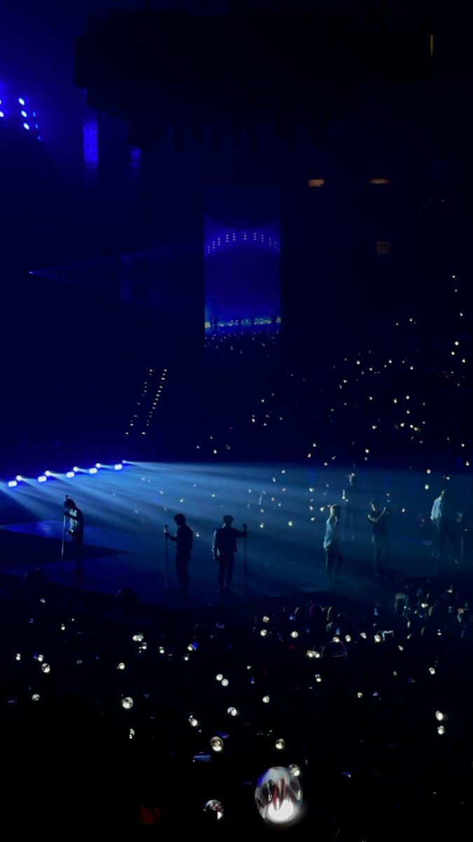 a group of people standing on top of a stage under blue lights in the dark