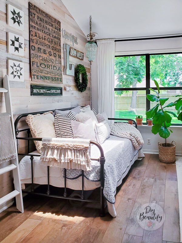 a bedroom with white walls and wood flooring has a bed, ladder, potted plant, and window in the corner